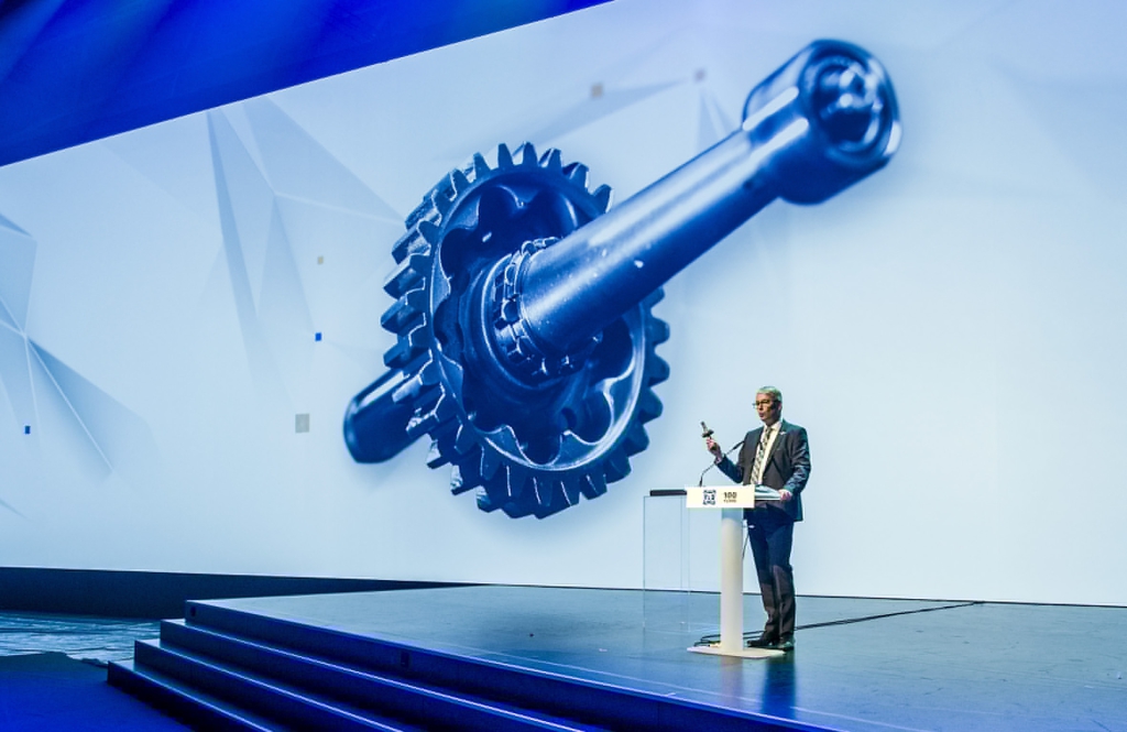 Dr. Stefan Sommer, Vorstandsvorsitzender der ZF Friedrichshafen AG, begrüßt die etwa 1500 Gäste zum Festakt 100 Jahre ZF. Der Abend bietet eine multimediale Zeitreise durch hundert Jahre Mobilitätsgeschichte weltweit. In der Hand hält er ein Zahnrad aus einem Soden-Getriebe für Pkw aus dem Jahre 1921.